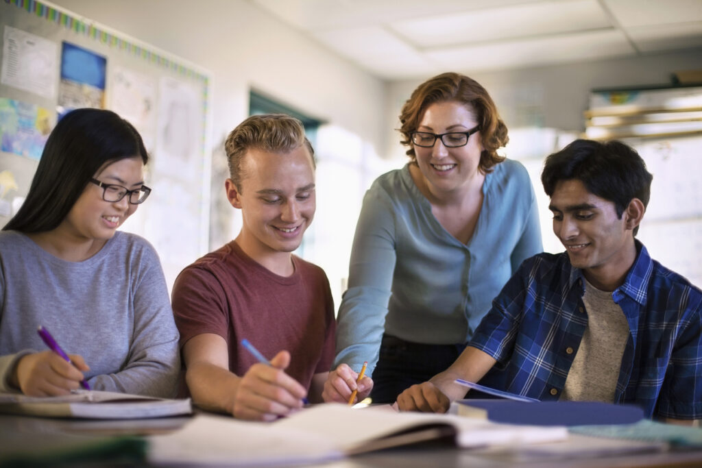 A female professor stood beside a table with a book, skillfully explaining lessons to her three attentive students.